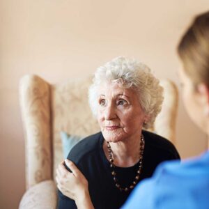 Family members sit beside an older adult in an assisted living room with hospice staff nearby.